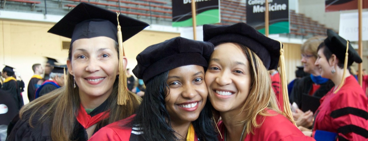 Two graduating doctoral students pose with their advisor at the hooding ceremony.